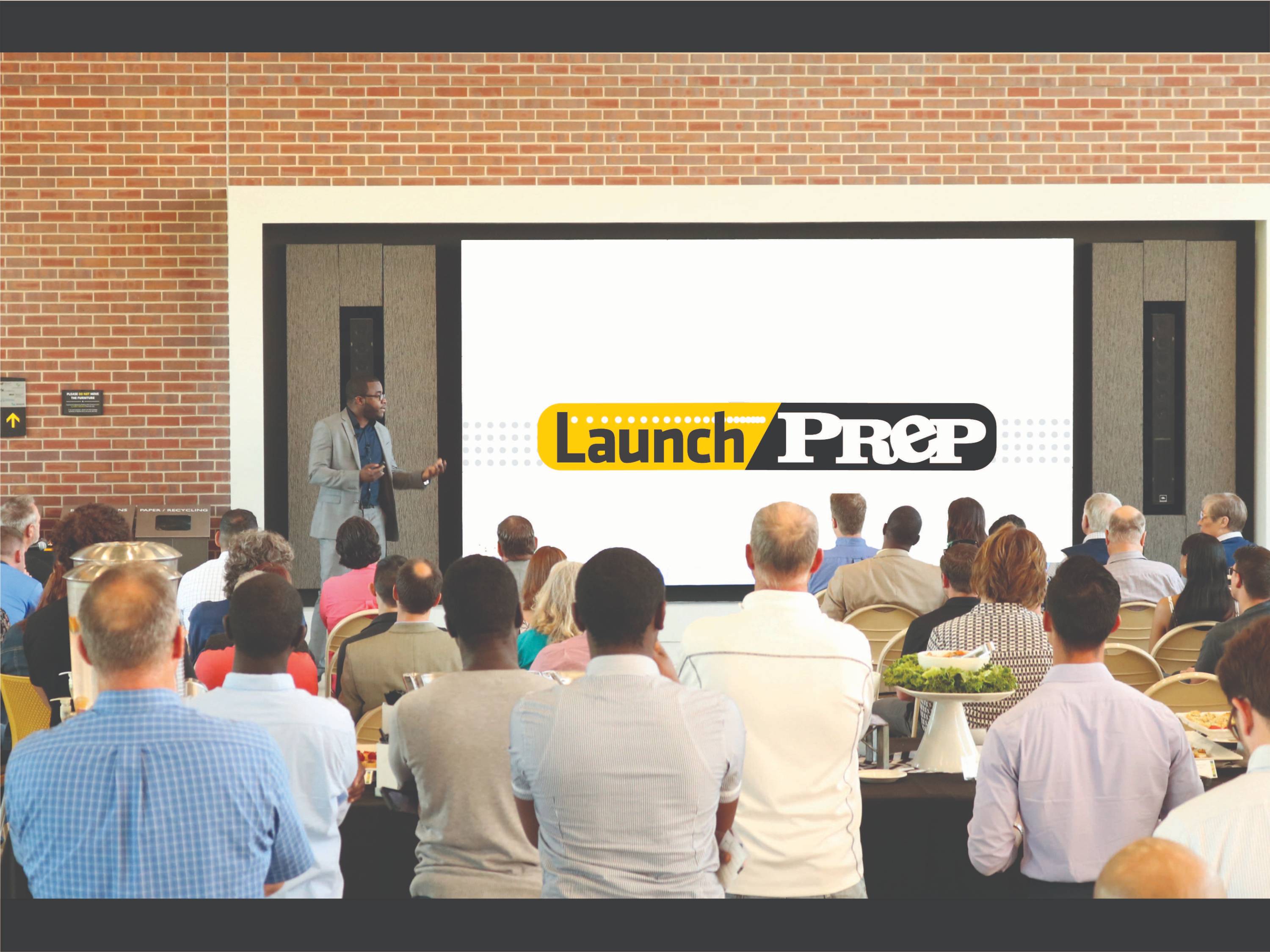 A man giving a presentation to an audience with launchprep logo. 