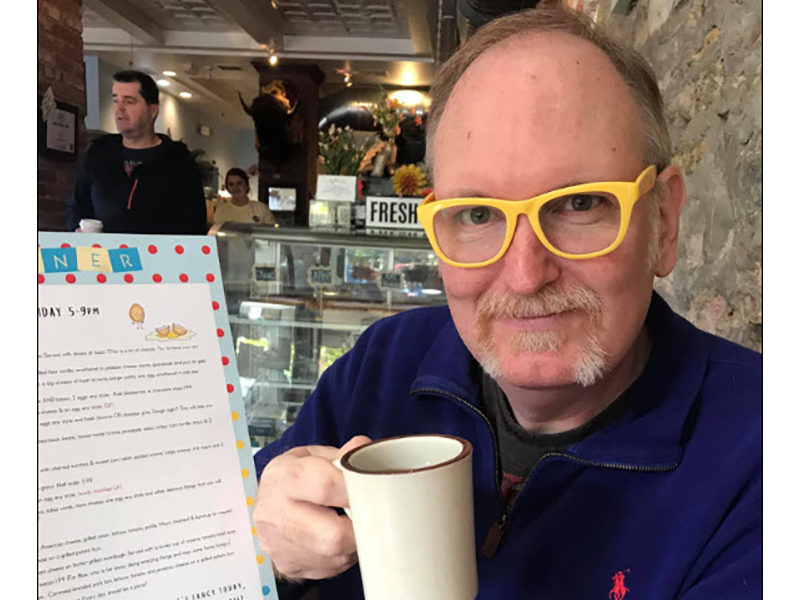 Darren Defrain wearing yellow frame glasses and holding a coffee mug
