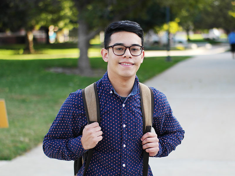 A student holding his backpack and smiling.