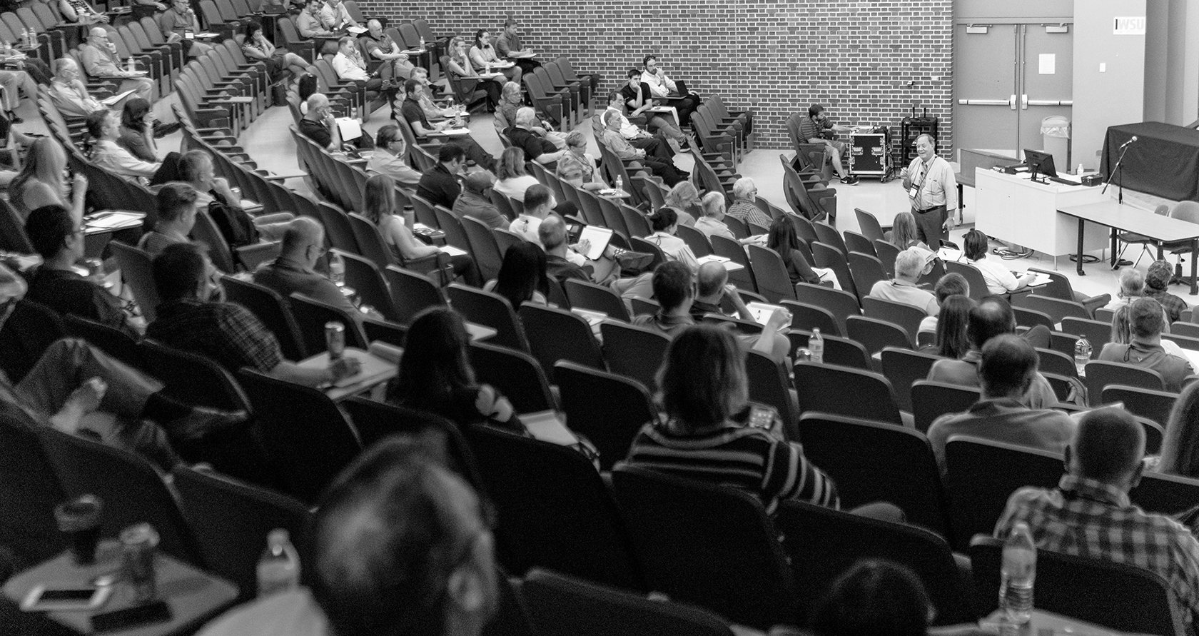 black and white photo of tiered lecture hall during conference lecture