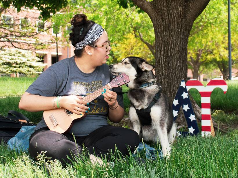 Female student playing ukulele to her dog.