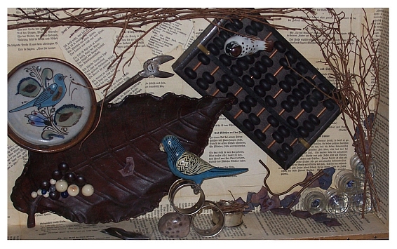 Photo displaying an art piece featuring ceramic bluebirds, an abacus, and various twigs on a backdrop of book pages. 