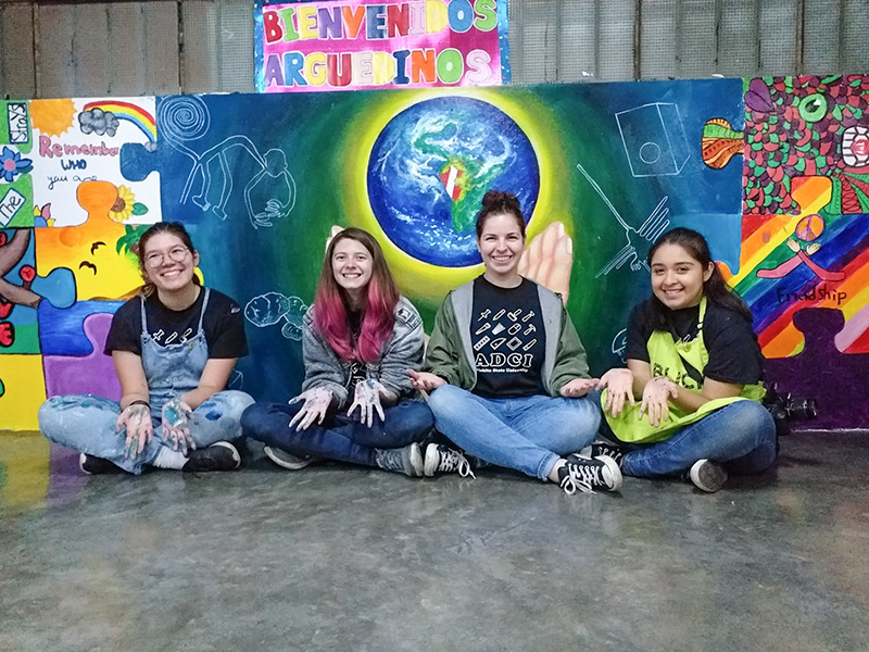 Celine, Bishop, Haley and Lily sitting in front of their mural.