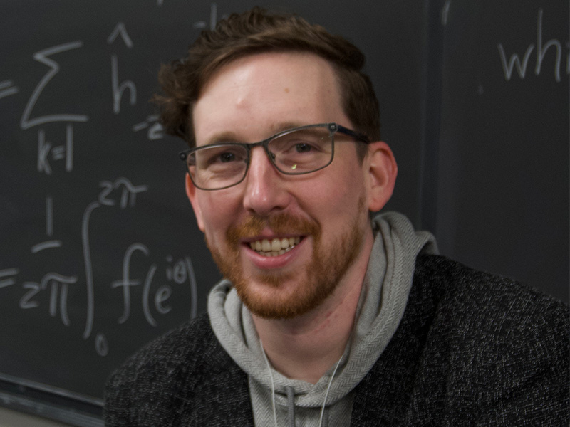 Trevor Mathew posed in front of a blackboard filled with calculations.