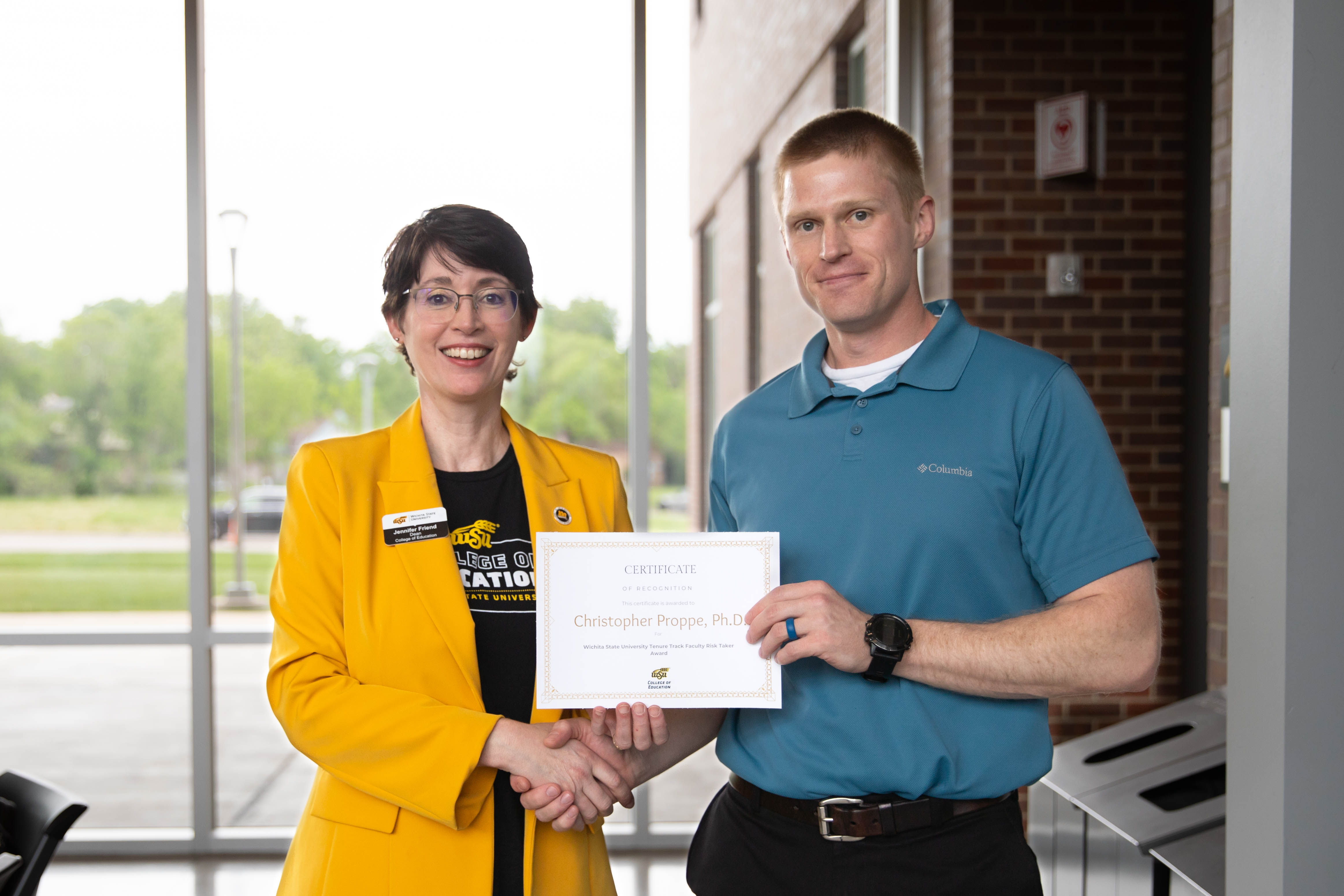Dr. Chris Proppe holds a certificate while shaking hands with Dr. Jennifer Friend, dean of the College of Education.