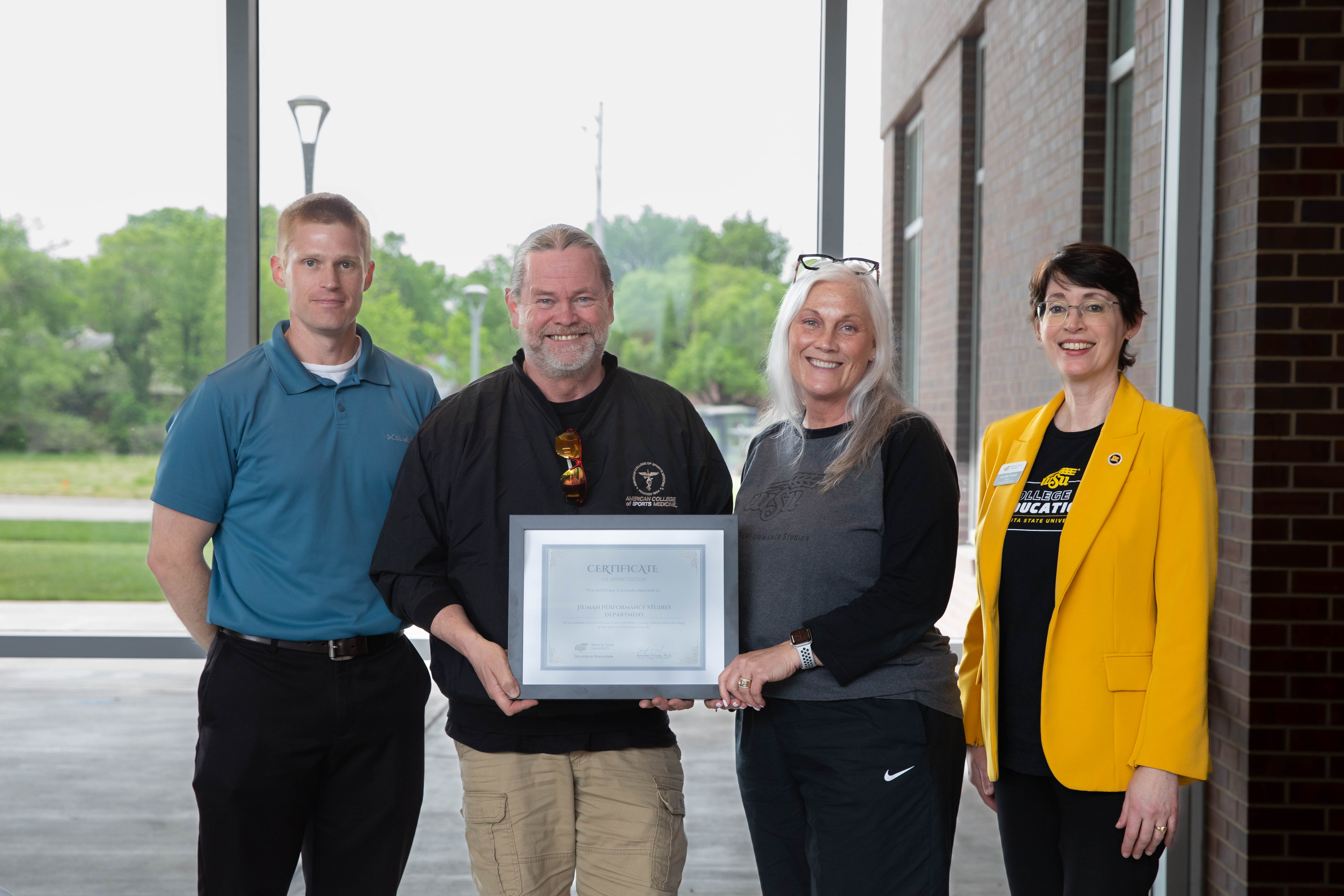 Faculty and staff from the Human Performance Studies Department hold a recognition certificate while standing with Dr. Jennifer Friend, dean of the College of Education.