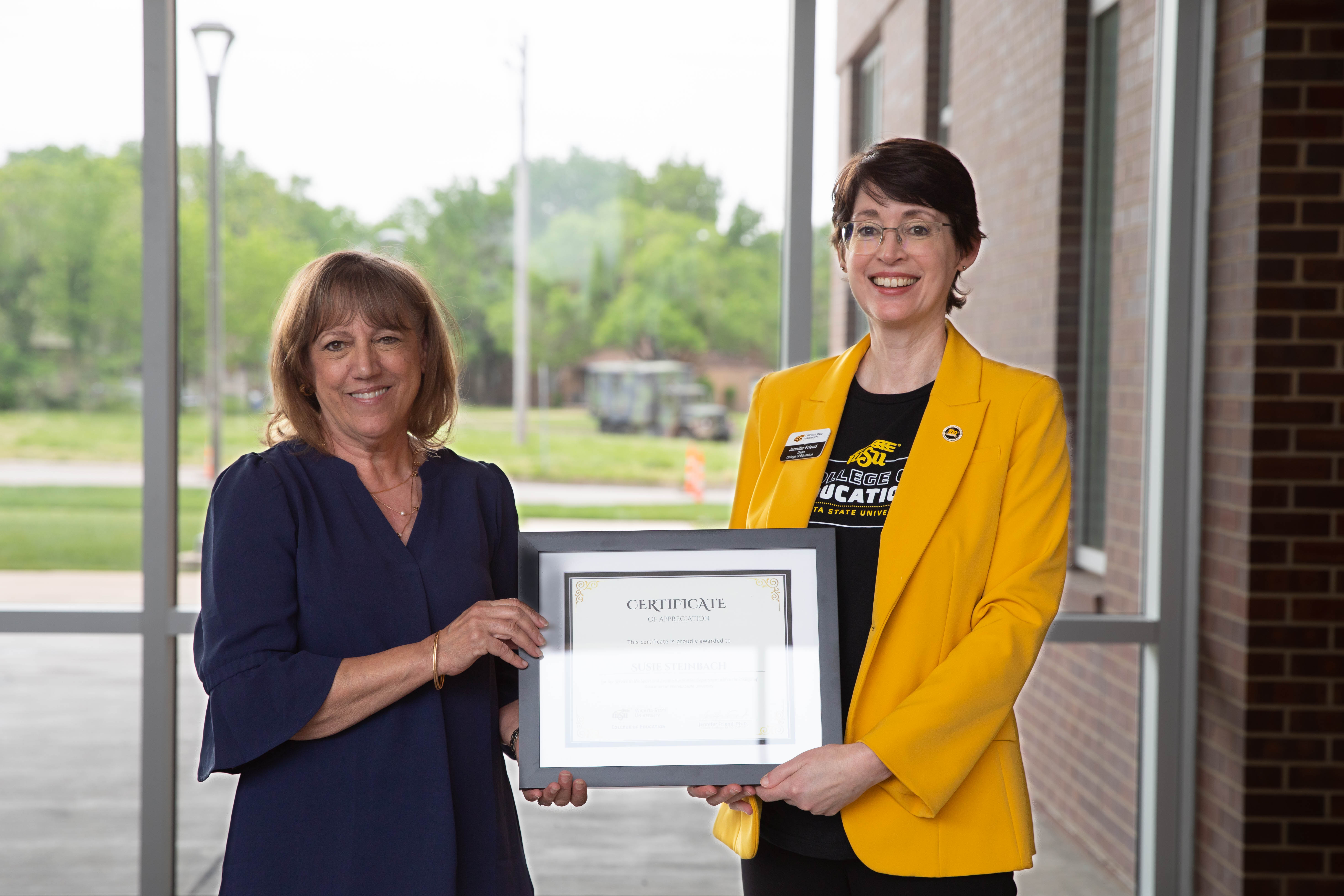 Susie Steinbach holds a framed certificate during her retirement recognition alongside Dr. Jennifer Friend, dean of the College of Education.