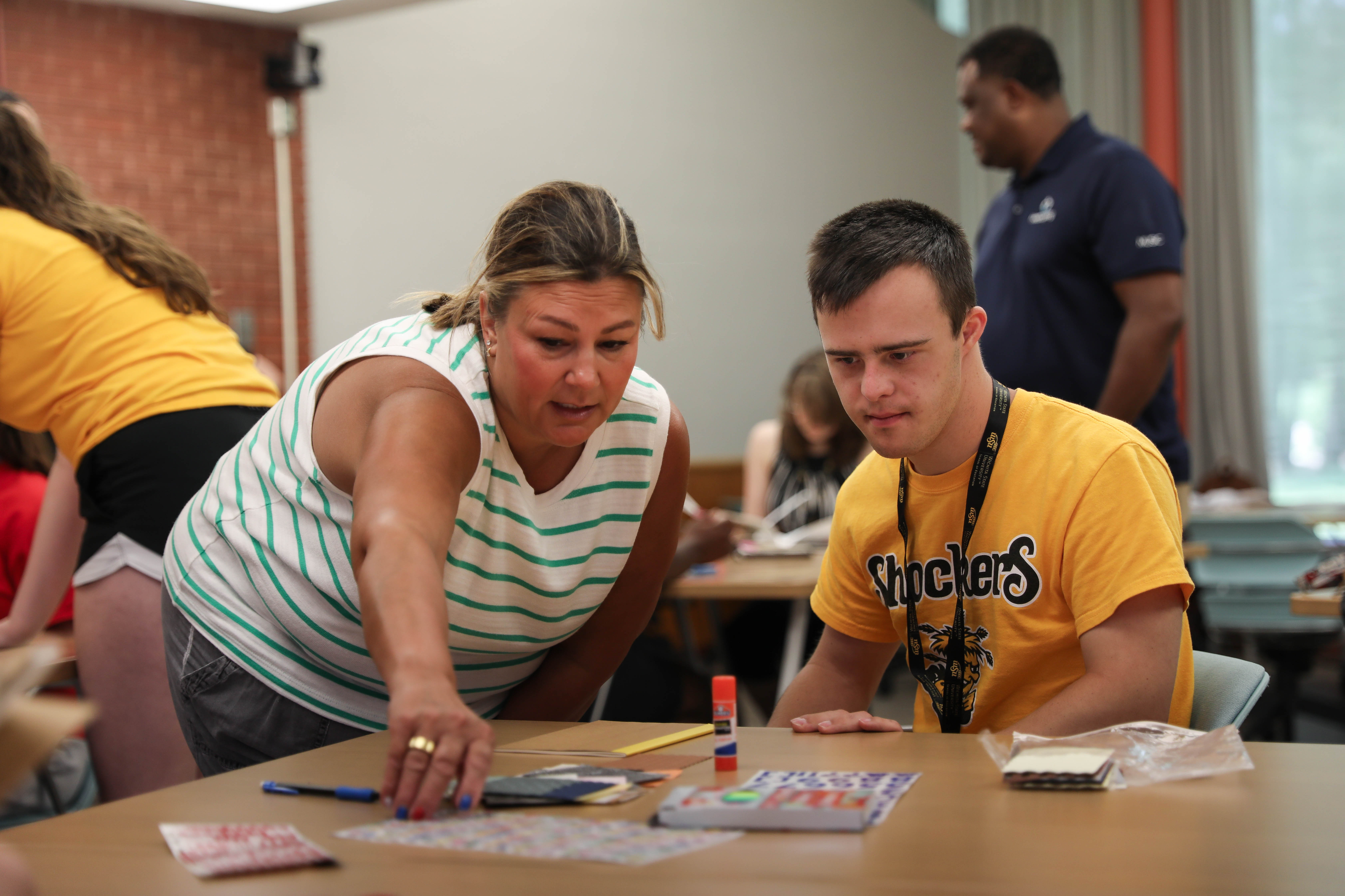 A Wichita State LIFE summer camp participant works on an art project with guidance from a camp mentor.