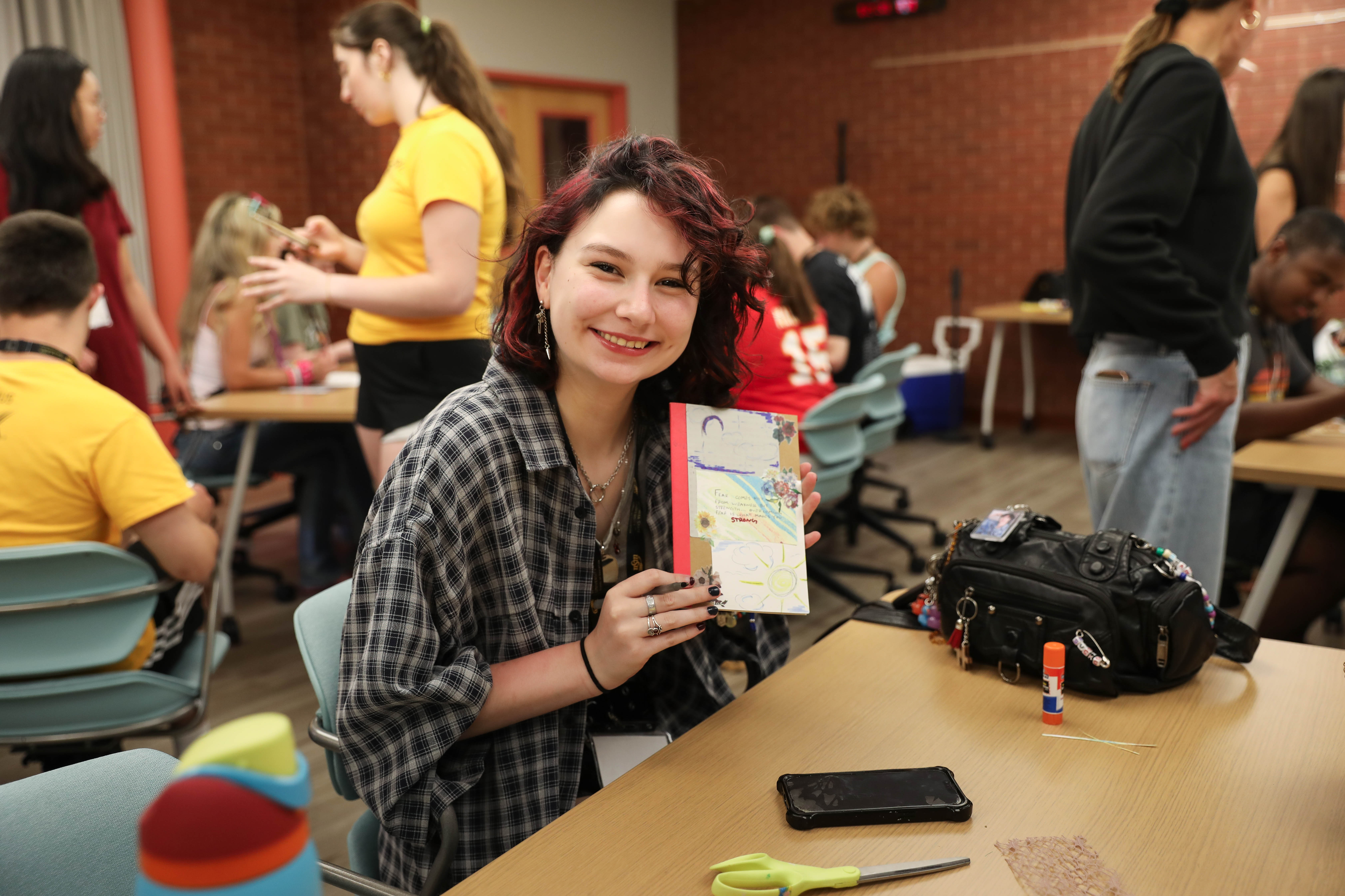 A Wichita State LIFE summer camp participant holds an art project while other participants work on activities at Wichita State University.