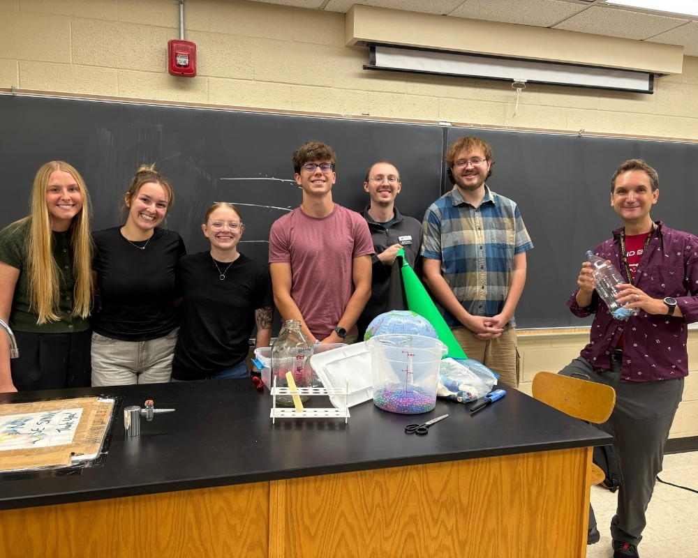 Six WSU science education students and Dr. Danny Bergman stand together behind a table of science demonstration materials at the KATS conference.