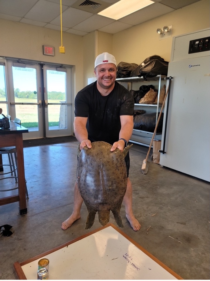 Studnet holding a large turtle by the back of its shell. The student is smiling at the camera.