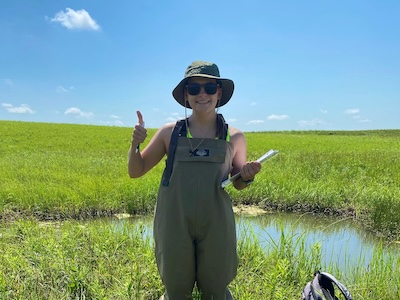 Student standing in field, wearing waders and smiling at camera.