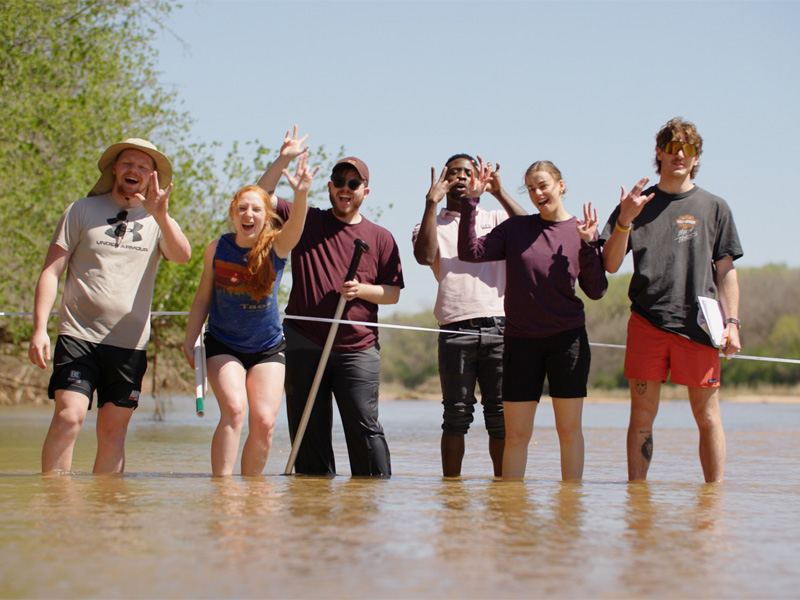 Students give up the Shocker hand sign in the middle of a river