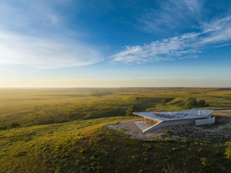 A landscape slightly behind and above the Youngmeyer Ranch Reserve building. Grassy hills stretch off into the distant as the sun is just slightly off-screen