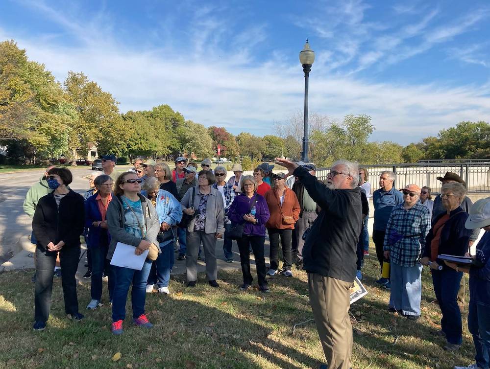 Photo of the Riverside walking tour. A group of people watch on as the history of an area feature not in camera view is discussed.