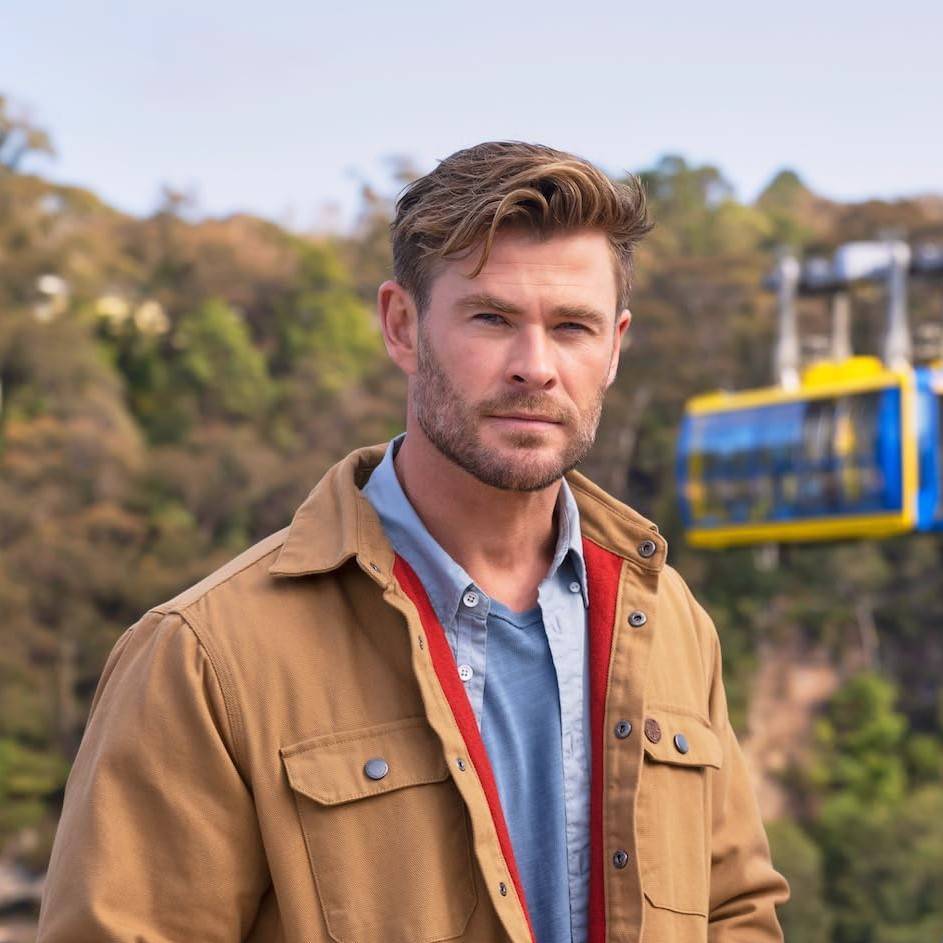 Chris Hemsworth smiling at the camera with a nature background.