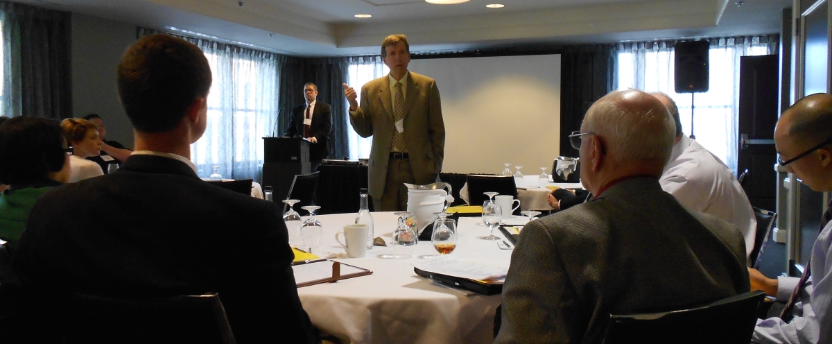 A man speaks to a roomful of people gathered around a table