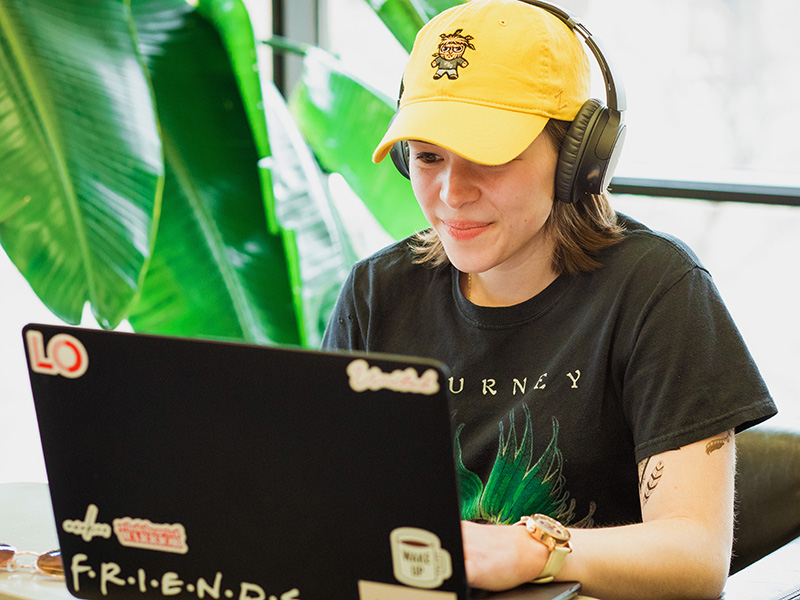 WSU student working on laptop on campus while wearing a Shocker hat and headphones