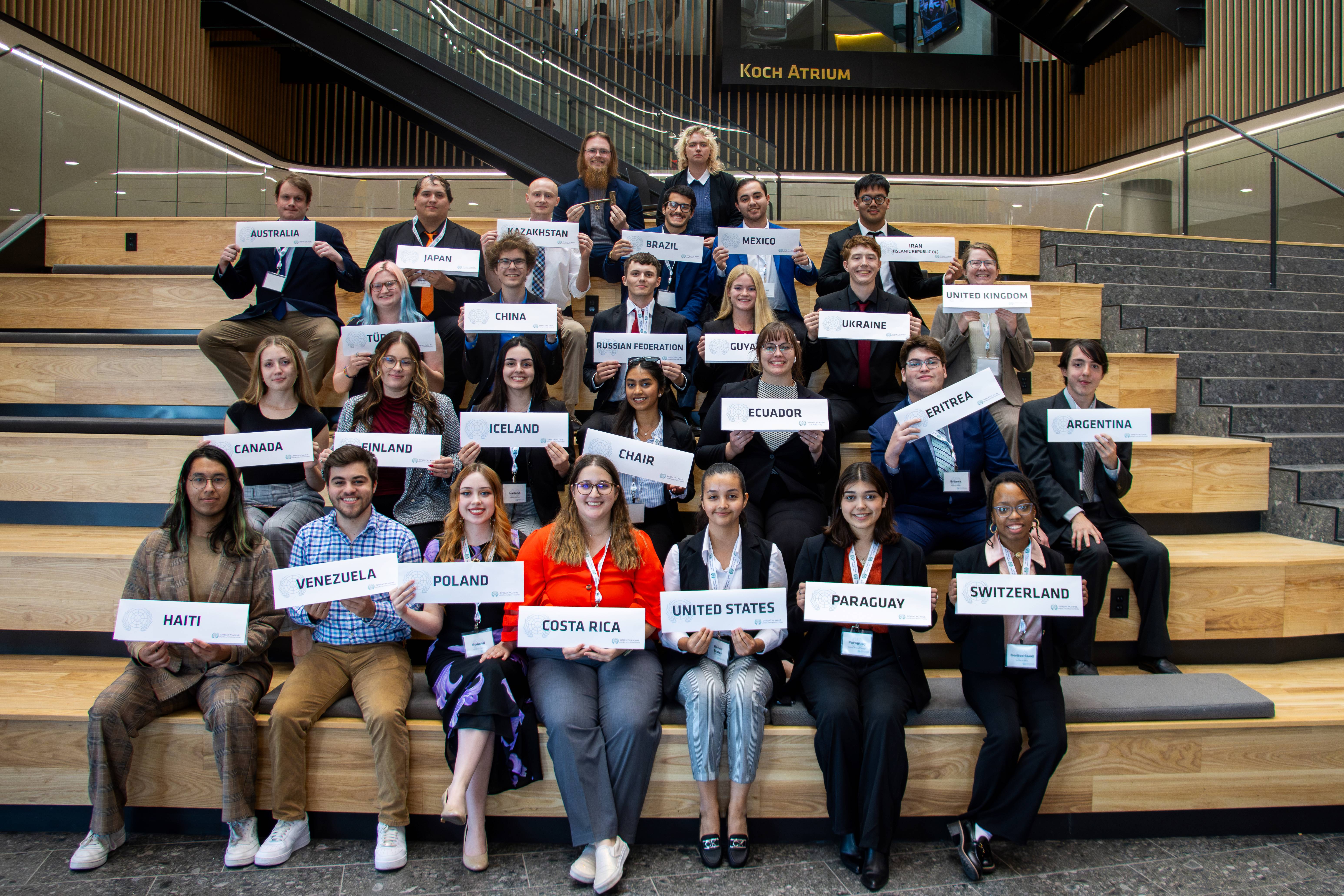A group of students on bleachers holding signs with their country designation
