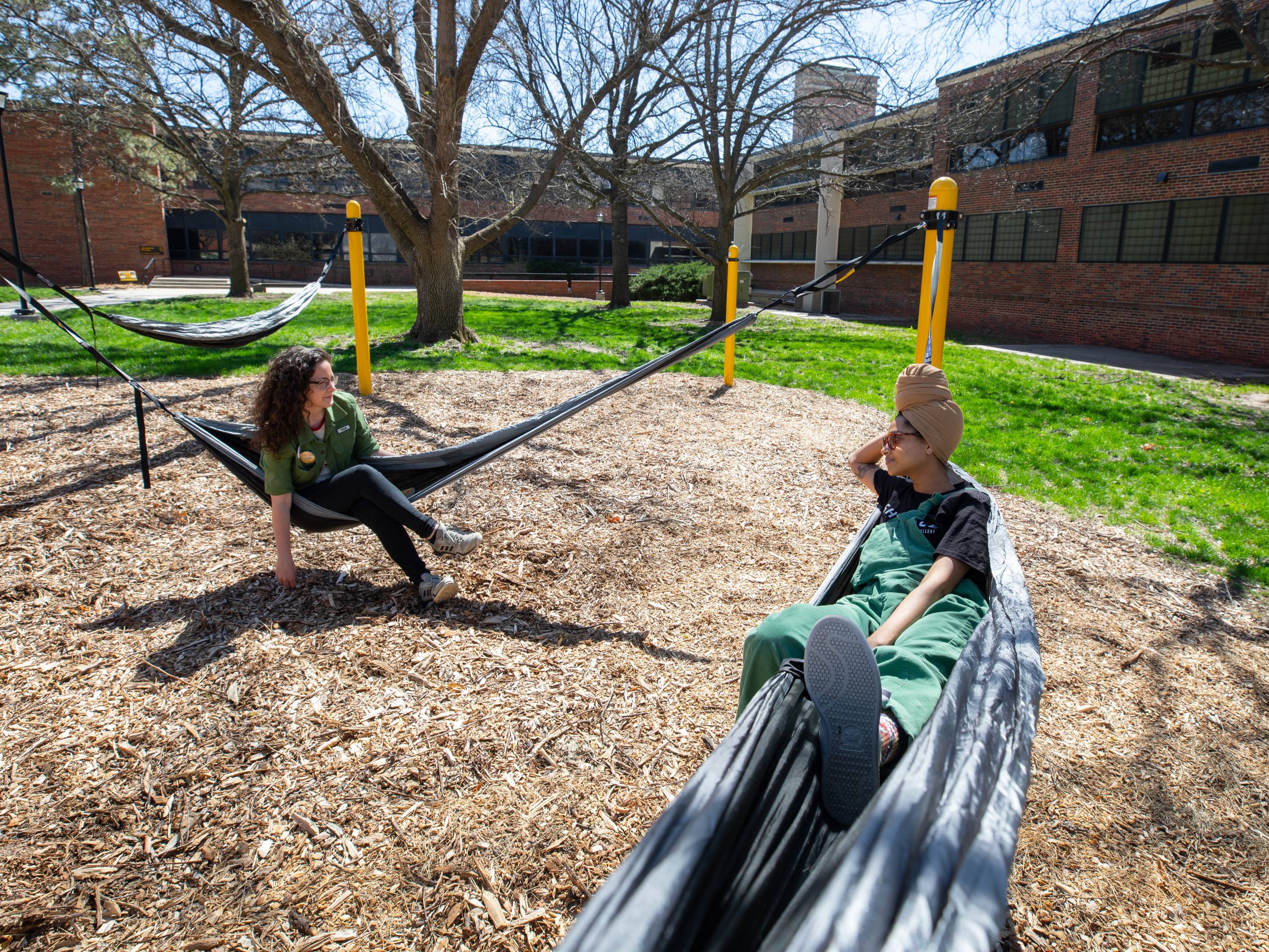 Two students relax in hammocks on campus.