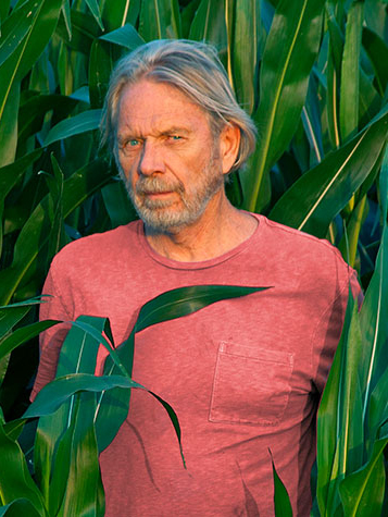 Bust photograph of Larry Schwarm standing in a feild of corn with a salmon colored shirt on.