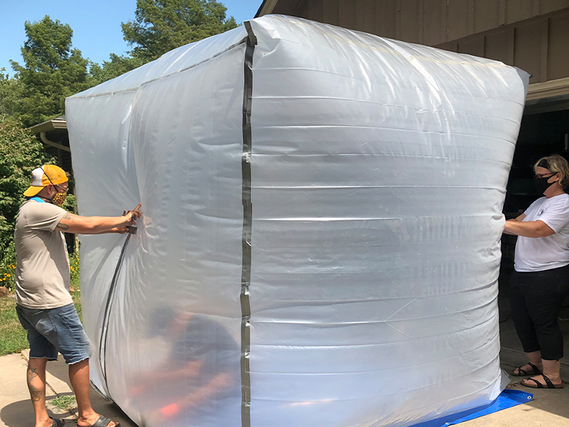 Two people stand beside an inflated square bubble.
