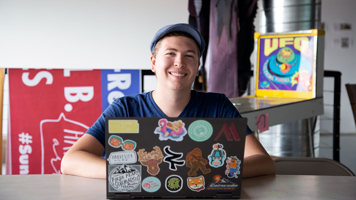 Nicklaus Lawrence smiles behind his sticker-covered laptop before a meeting of the ShiftSpace Student Group.