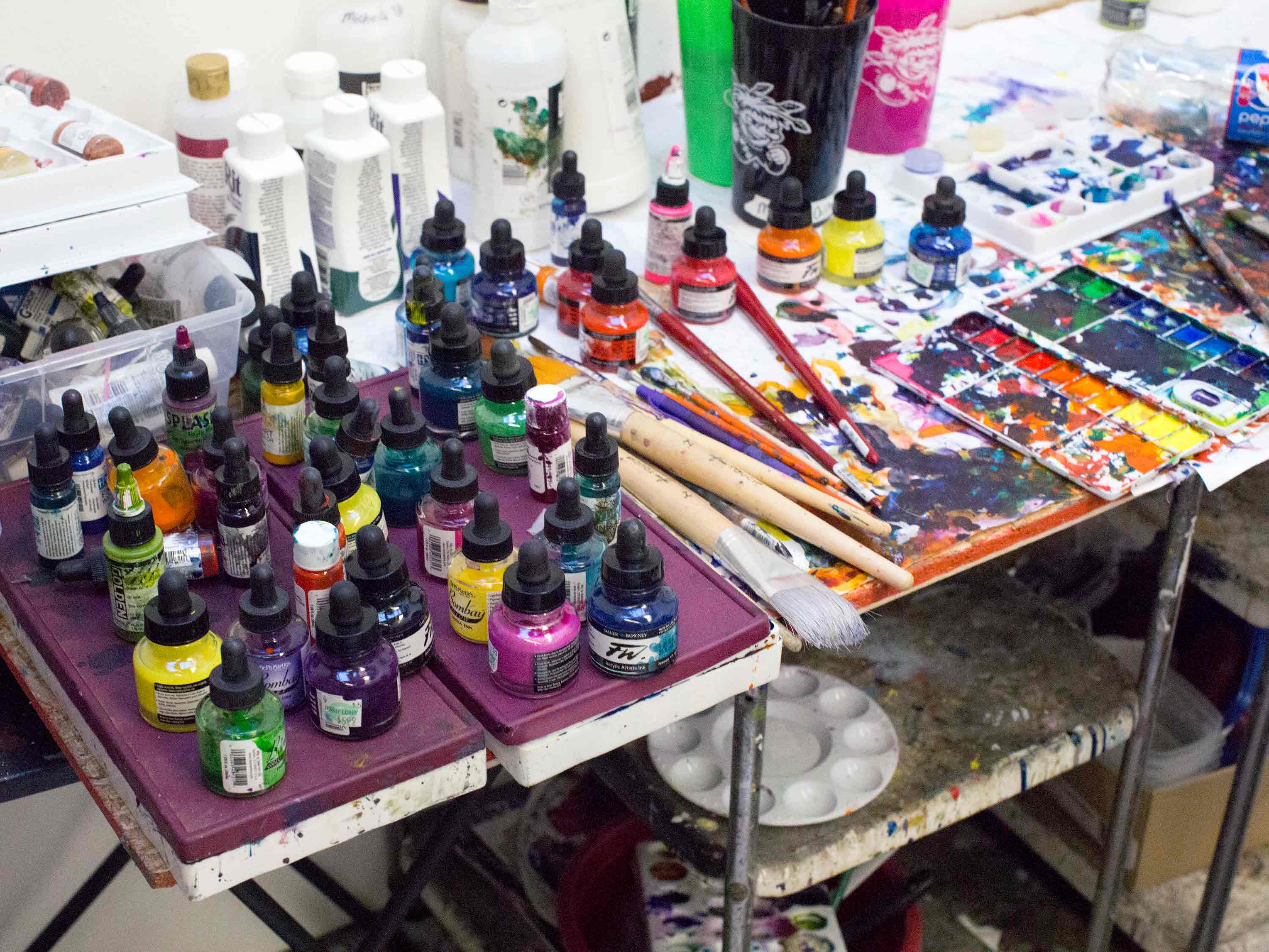 A photo of a cart covered in paint, brushes and other art supplies.