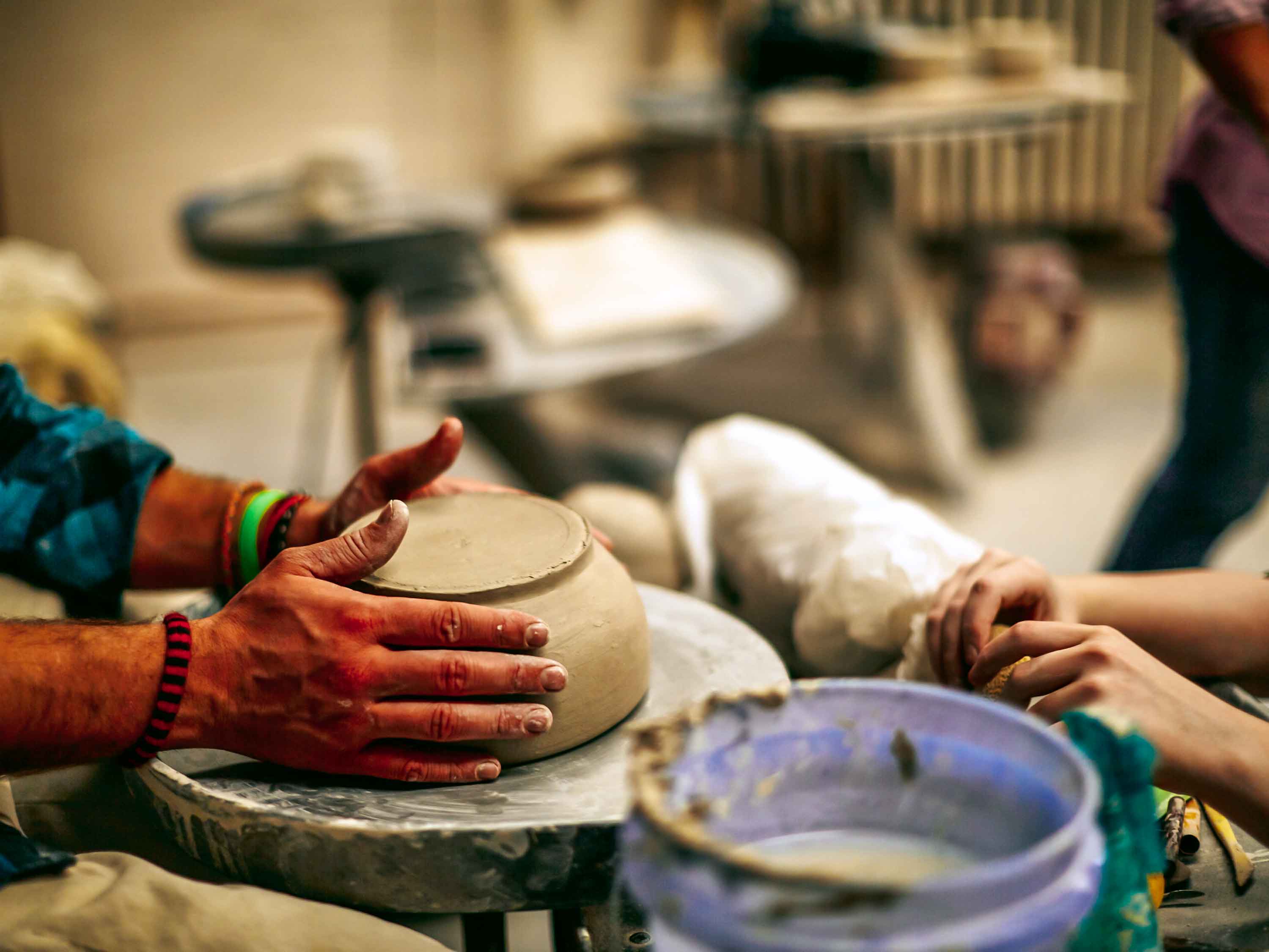 Two pairs of hands are pictured molding clay on a pottery wheel. 