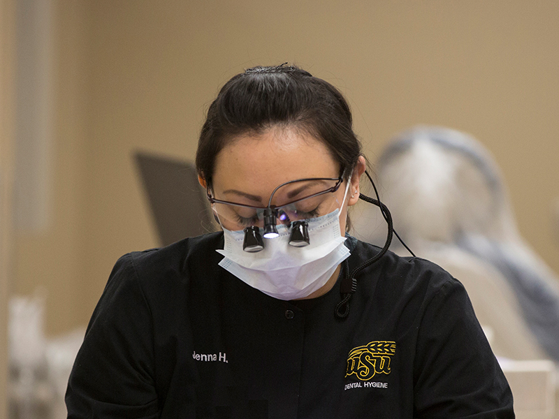 dental hygiene Dental hygiene student looks down through magnification loupes