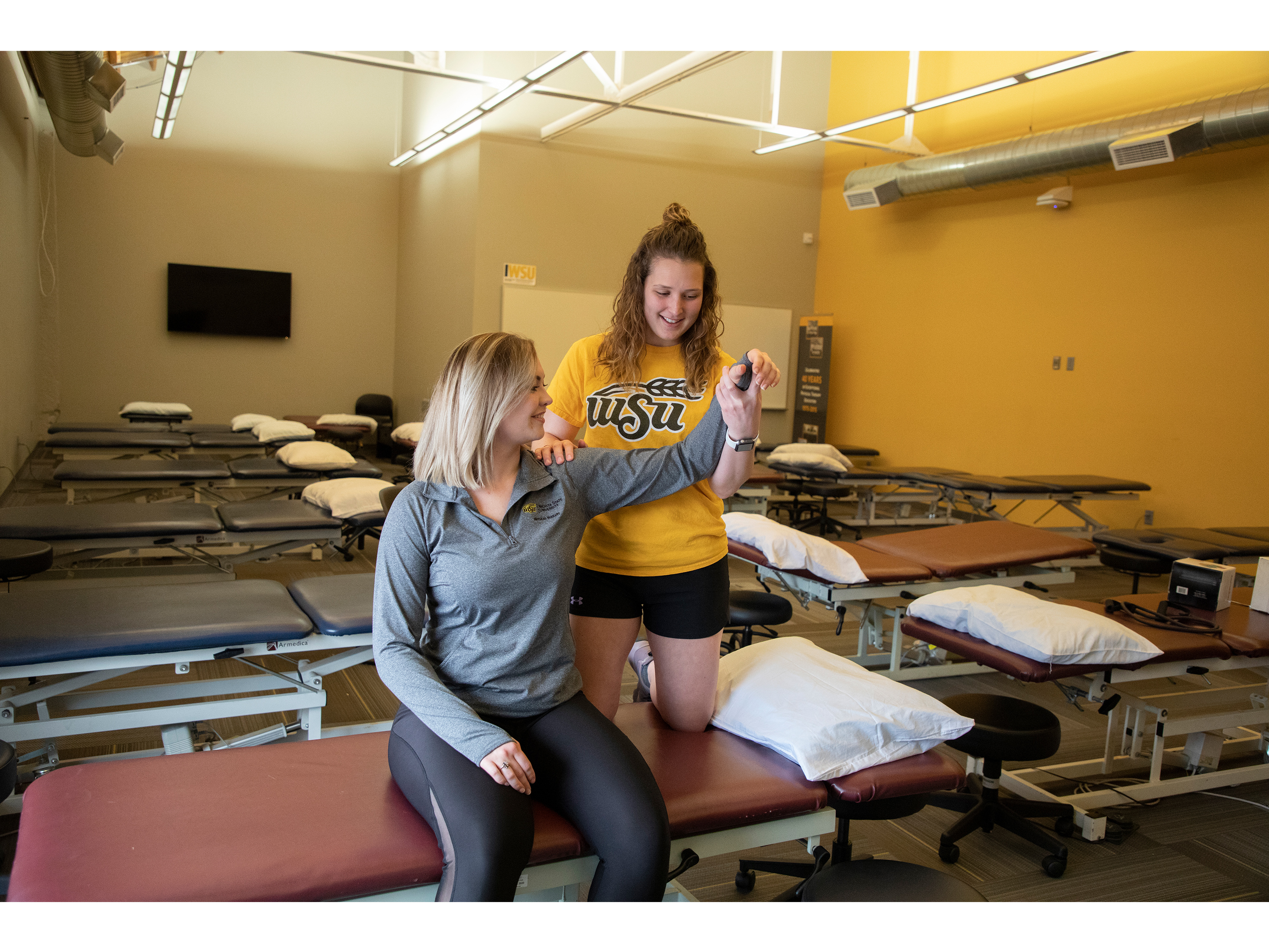Two Physical therapy students engage in a physical therapy exercise in a well-equipped therapy room.