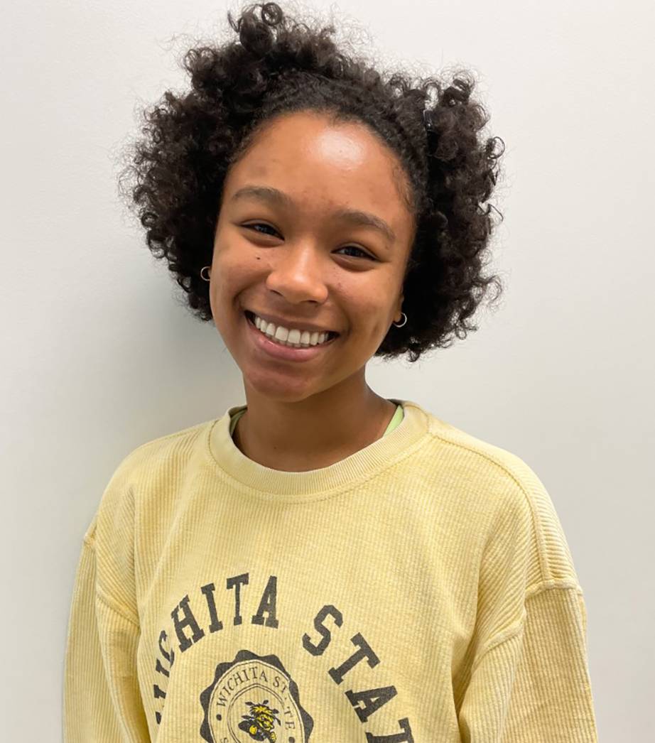 Honors student Ayshea Banes posing for a headshot photo. Ayshea is wearing a light yellow Wichita State sweatshirt and silver hoop earrings. She is smiling and looking directly into the camera.
