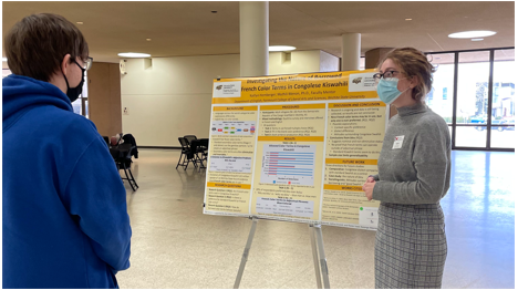 Student standing in front of her research poster and speaking with another individual