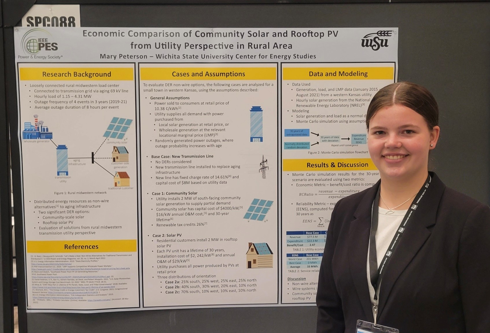 Honors student Mary Peterson posing for a photo with her research poster. She is wearing a black blazer with a white whirt and a conference lanyard around her neck. She is smiling and looking directly into the camera.
