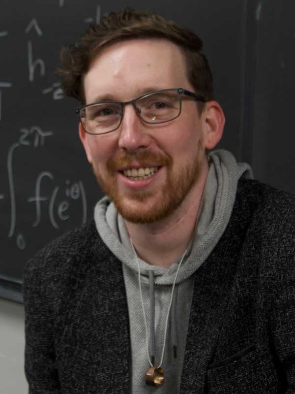 Mathew Tucker posed in front of a blackboard filled with equations.