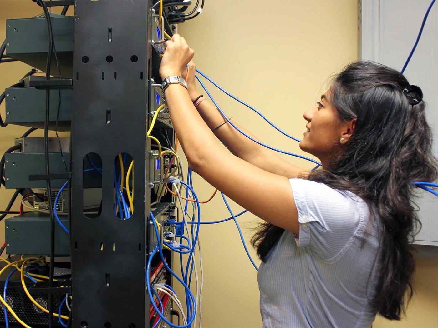 Female student running and inserting networking cables into a server. 