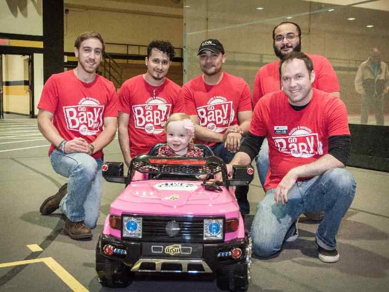 Mechanical Engineering students pose by a toy car designed for Go Baby Go 
