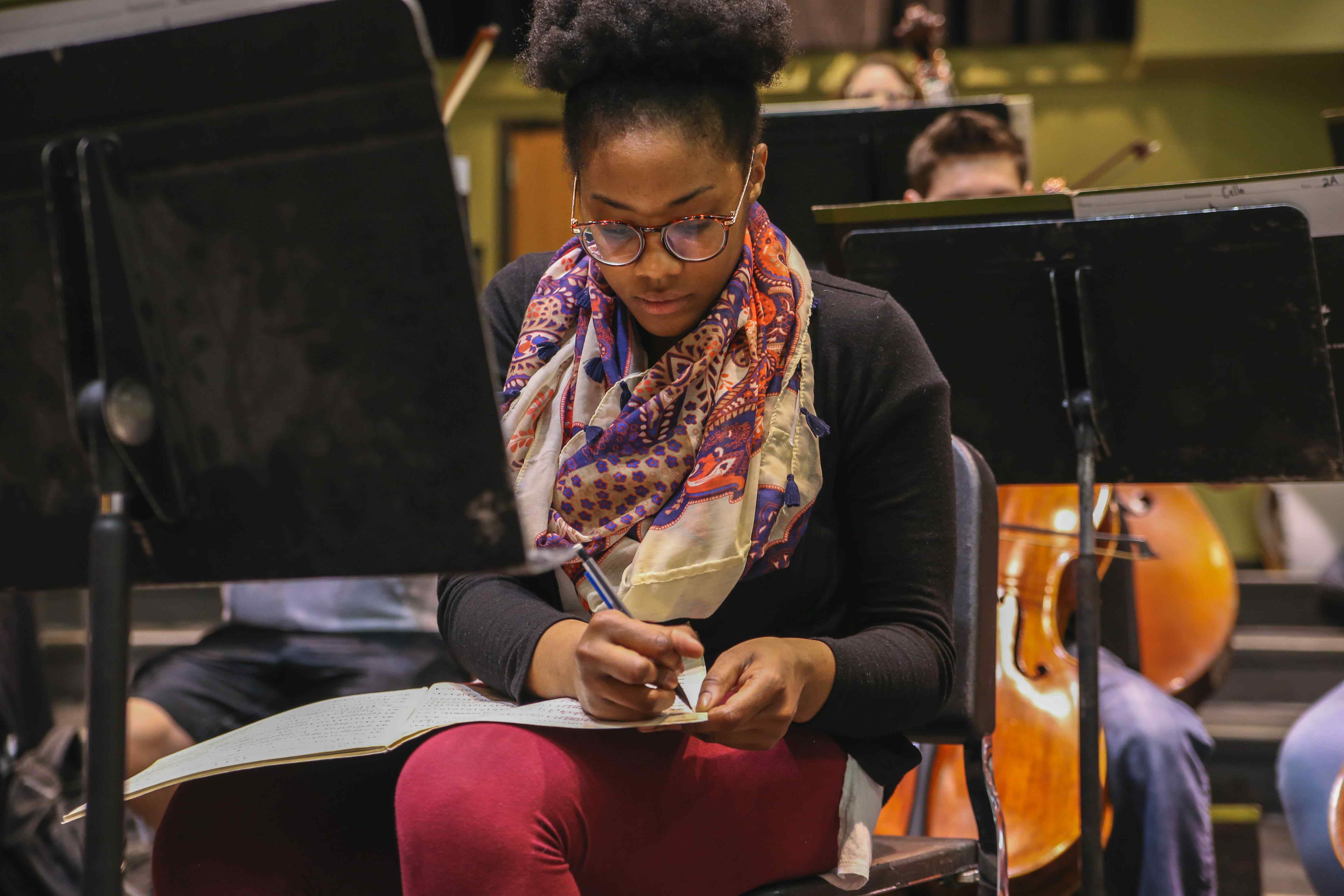 Female music student taking notes during rehearsal.