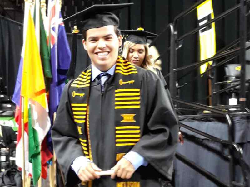 A graduate crosses the stage with his Spanish degree at commencement