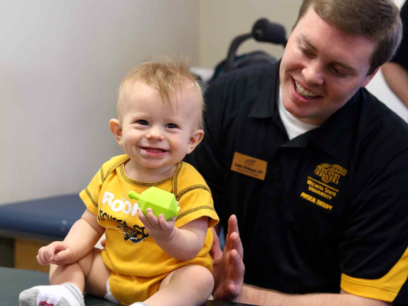 Baby smiling while playing with male WSU student.