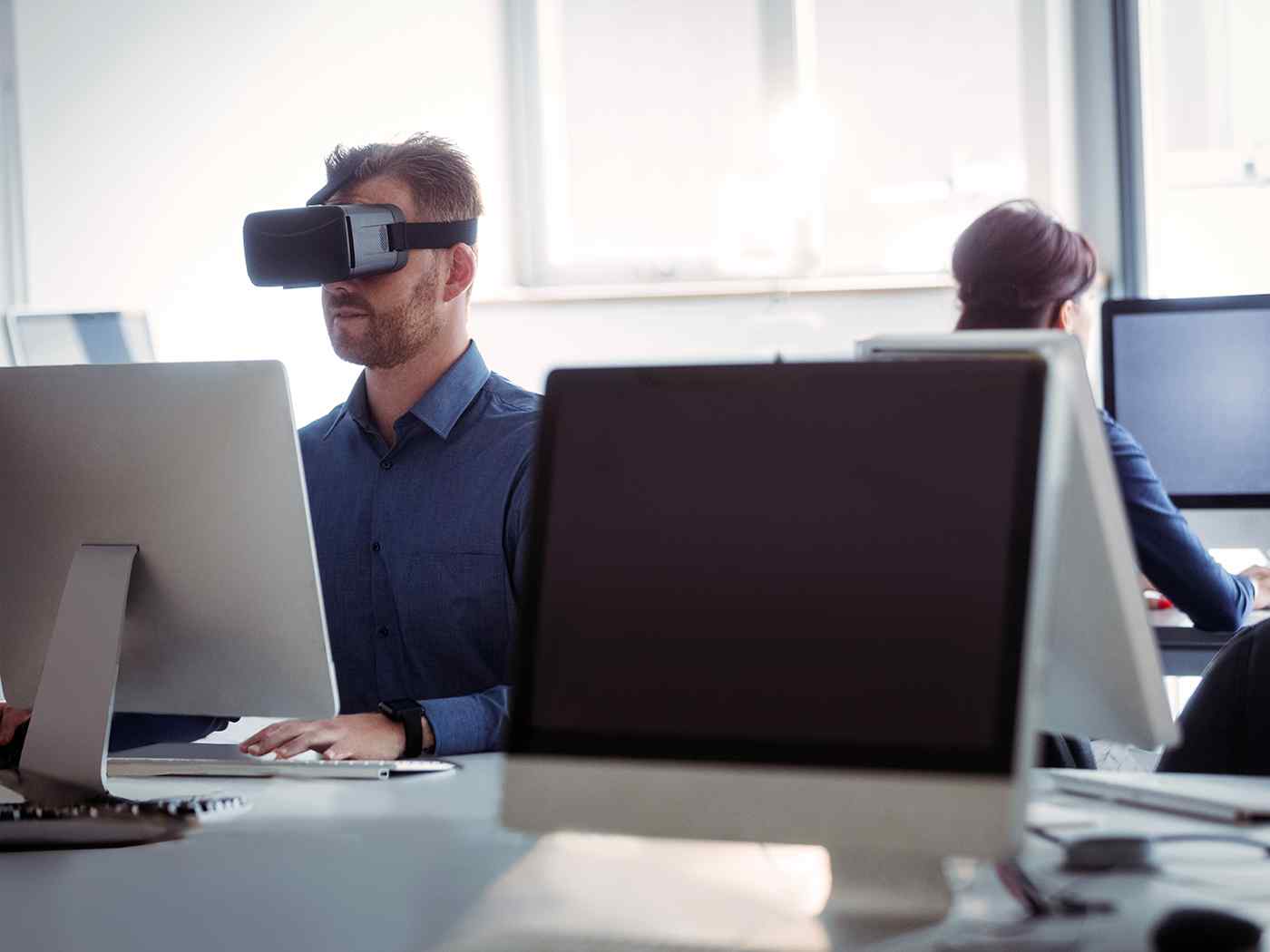 Game design student wearing Virtual Reality headset while working on a computer.