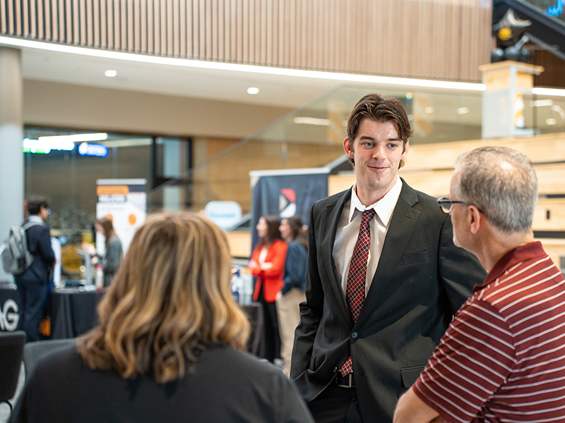 A management student talks to business professionals at a networking fair in Woolsey Hall.