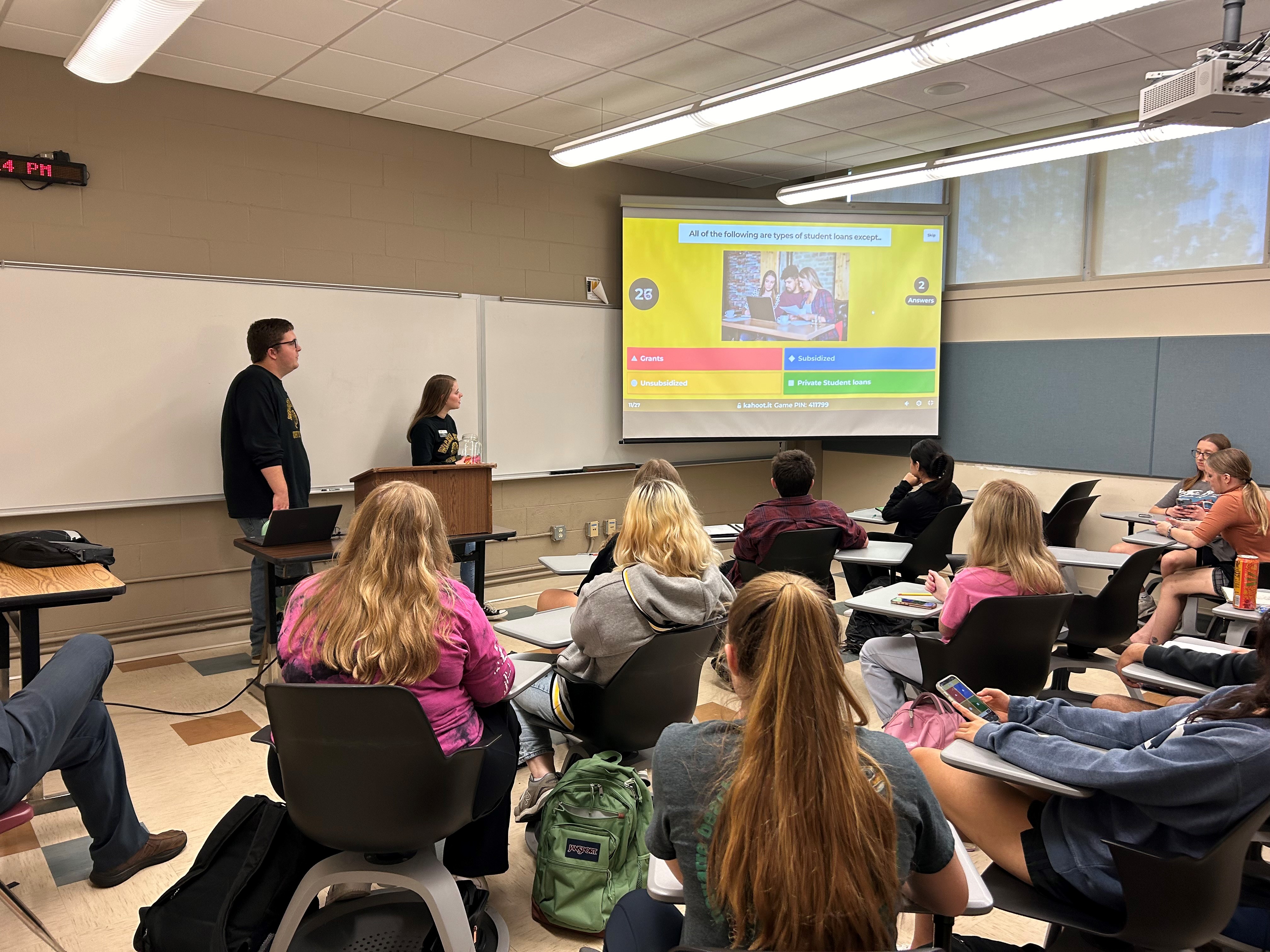 A photo of two Shocker Financial Wellness Peer Counselors presenting a Kahoot activity at a Financial Wellness student event. The students are engaged with the activity.