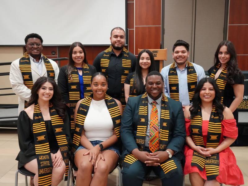 A group photo of Passage 2 Success graduates in the Rhatigan Student Center. There are two rows of students and these individuals are all wearing the same Diversity and Inclusion graduation stole.