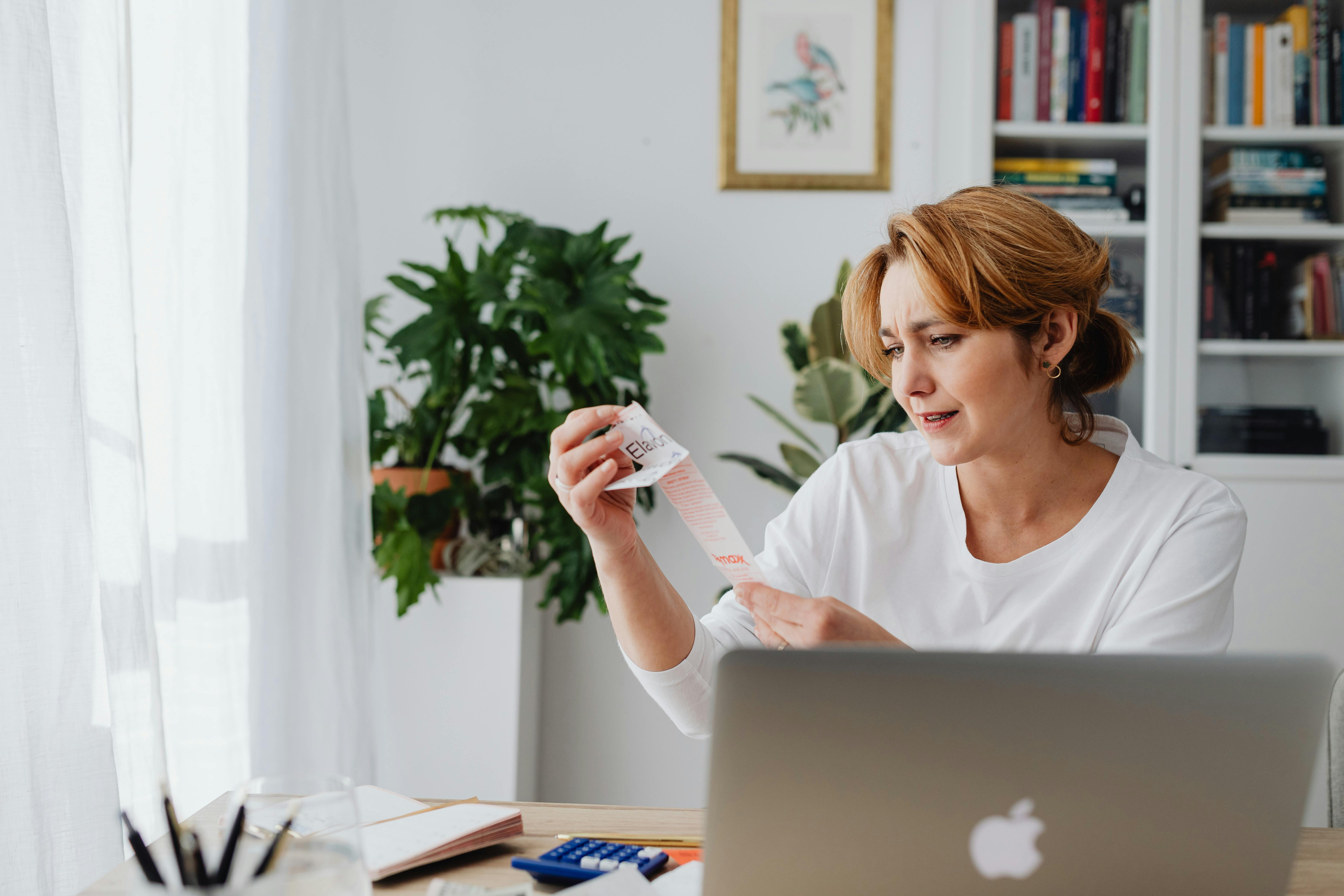 Woman sitting behind a desk using a laptop and reviewing a receipt.