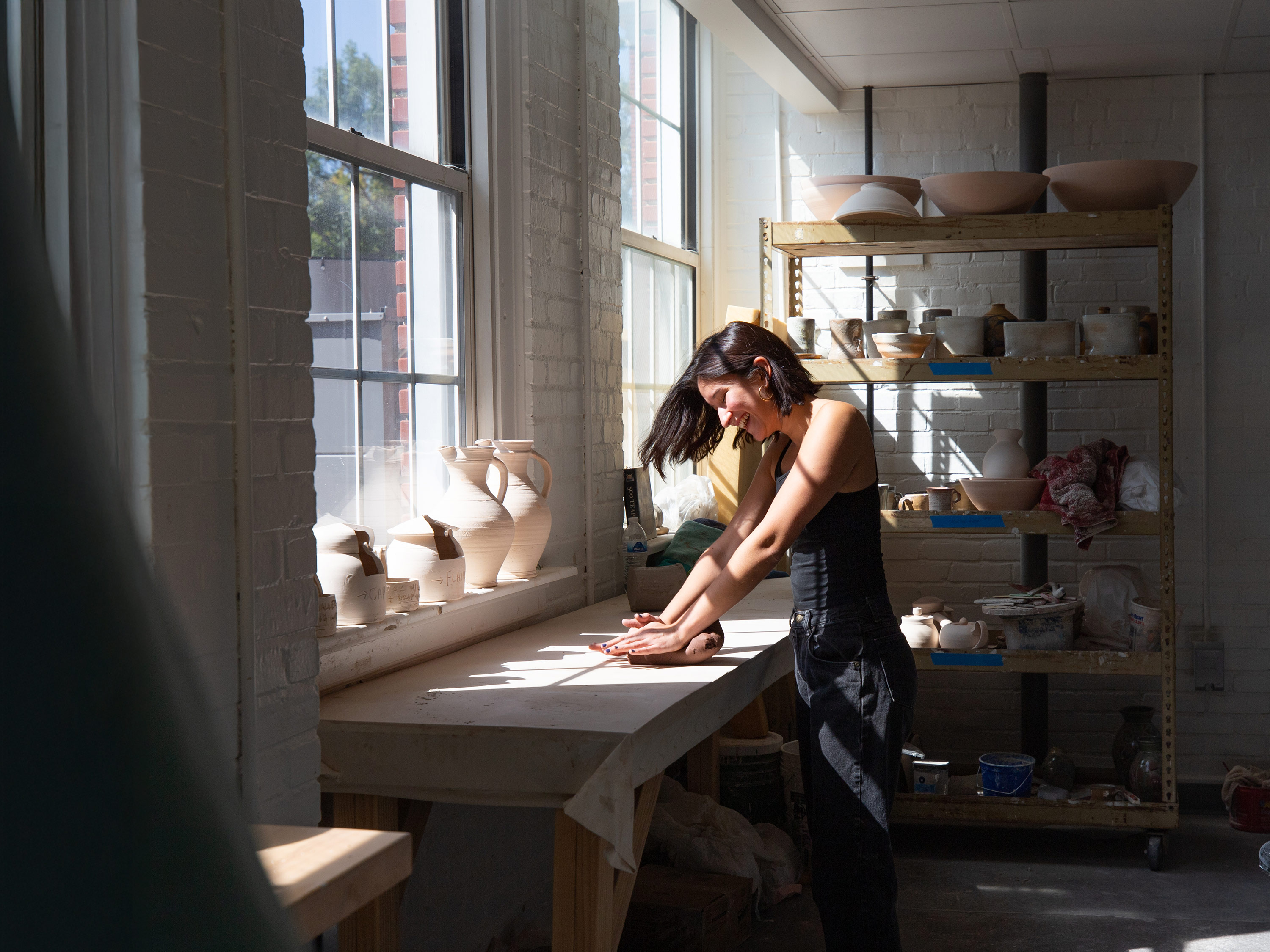 A graduate studio art major hand rolls clay in a ceramics studio.