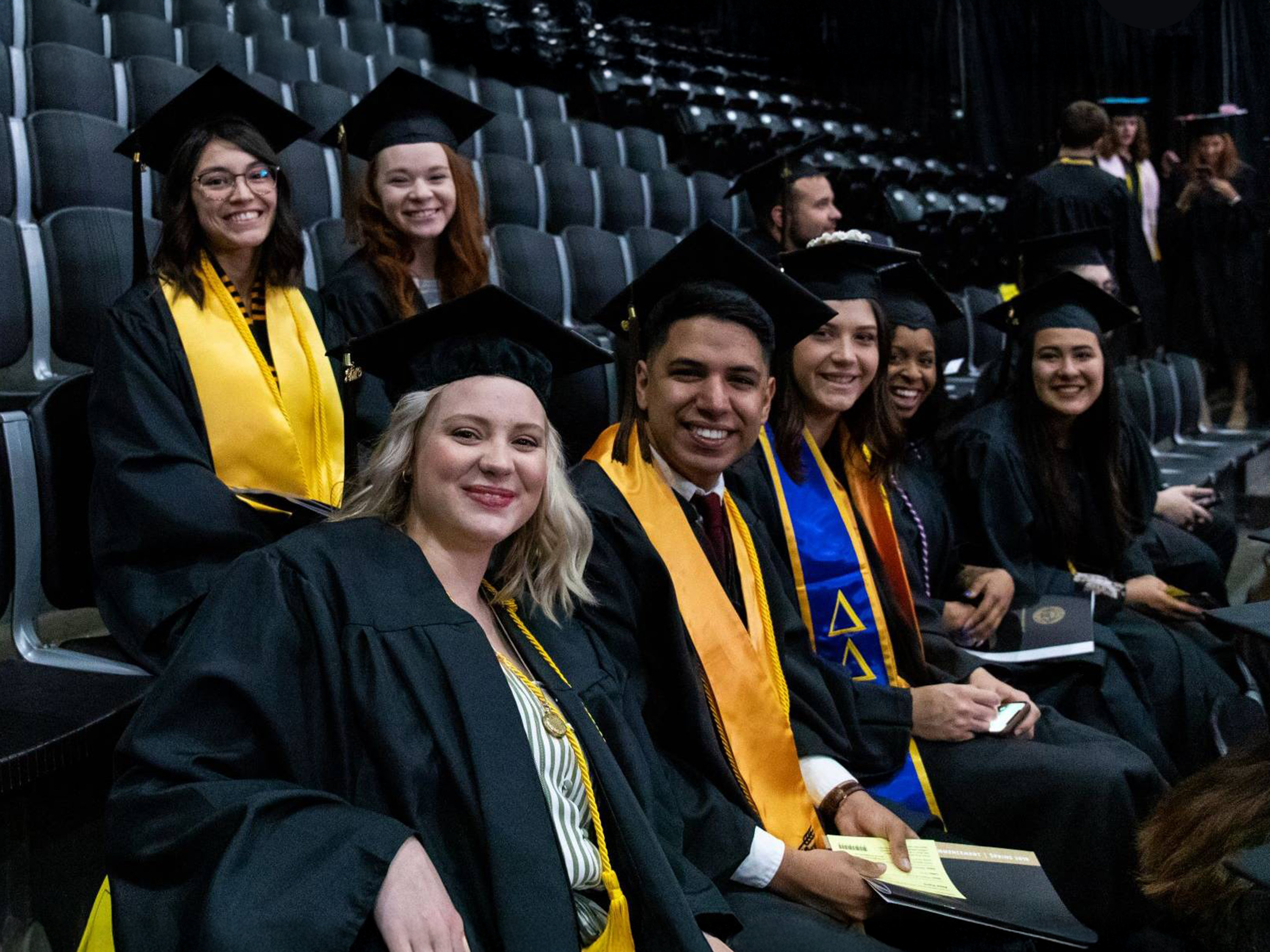 Smiling students seated in a group at spring commencement.