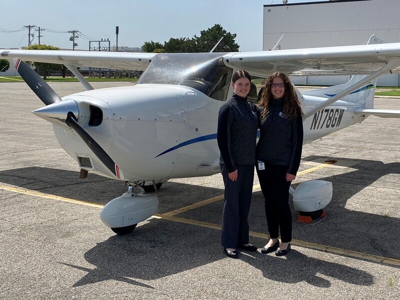 Mary and Grace Peterson stand in front of an airplane