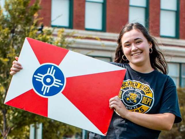 Claire holding the City of Wichita flag on campus at Wichita State