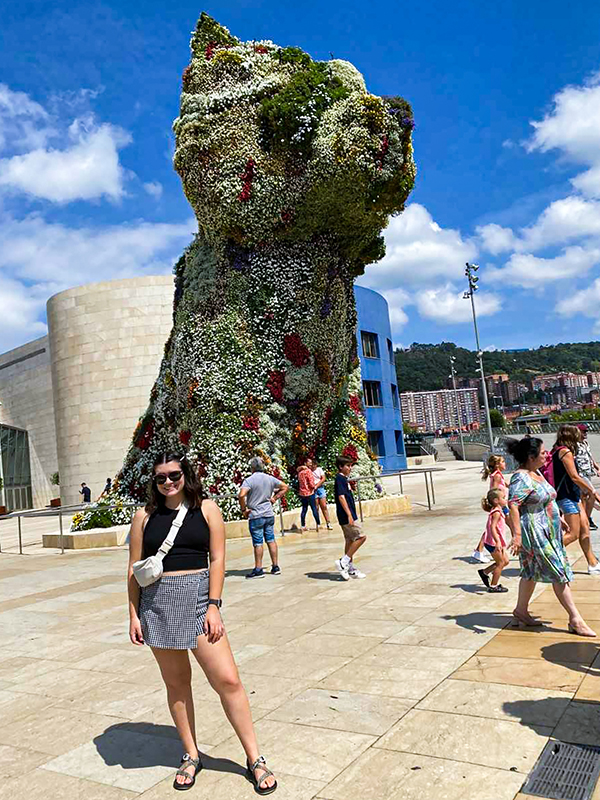 Nicole Bloomquist posing in front of "Puppy" by Jeff Koons in front of the Guggenheim Museum Bilbao.